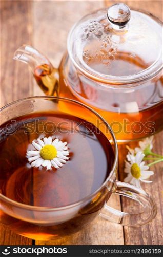 Herbal chamomile tea in glass cup and teapot with chamomile flowers on wooden table still life