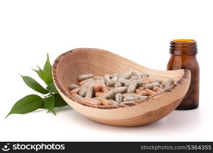 Herbal drug capsules in wooden plate isolated on white background cutout. Alternative medicine concept.