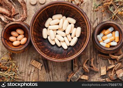 Herbal medical pills with healing plant on old wooden background.Alternative medicine tablets. Herbal medicine in pill