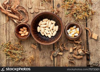 Herbal medical tablets with healing plant on wooden table.Alternative medicine tablets. Vitamins, tablets and pills