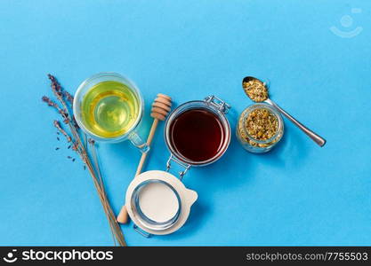 herbal medicine and health concept - close up of cup of chamomile tea, honey in glass jar with dipper and dry lavender flowers on blue background. cup of herbal tea, honey and dry chamomile flowers