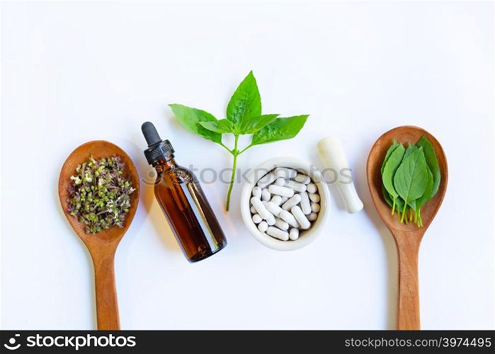Herbal medicine capsules pills and essentail oil with leave and flower of sweet basil on white