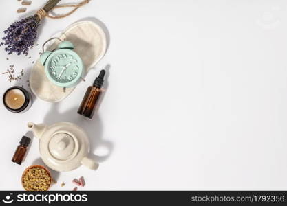 Herbal medicine for treat depression and insomnia concept. Alarm clock, sleep mask, medicine herbs, capsules, camomile tea and aromatherapy oil on white background, top view, copy space