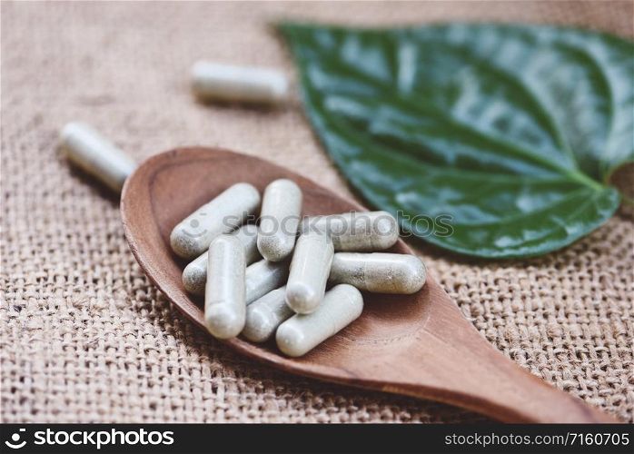 Herbal Medicines / Natural herb capsules on wooden spoon and green leaf on sack background , selective focus