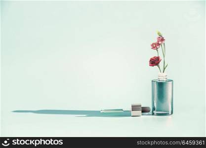 Herbal skin care cosmetics and beauty concept. Facial Serum or Oil bottle with dropper or pipette and flowers stand at blue background, front view. Modern minimal creative layout