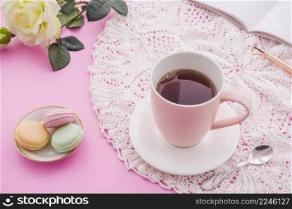 herbal tea cup with macaroons spoon rose pen book pink background