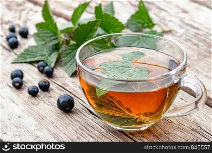 Herbal tea from currant leaves in a glass transparent cup on a wooden table near the green leaves and currant berries. Close-up.. Herbal tea from currant leaves in a glass transparent cup on a wooden table near the green leaves and currant berries.