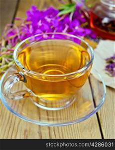 Herbal tea in a glass cup and teapot, fresh flowers fireweed, fireweed flowers dry on paper on a wooden boards background