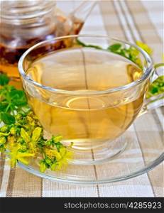 Herbal tea in a glass cup and teapot, fresh flowers tutsan on the linen tablecloth background