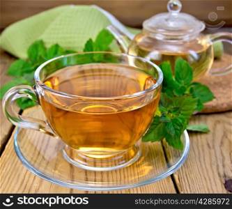 Herbal tea in a glass cup and teapot, fresh mint leaves, a napkin on a wooden boards background