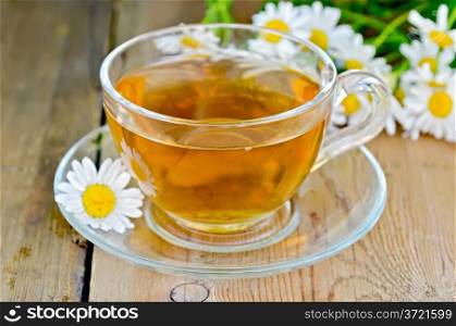 Herbal tea in a glass cup, fresh chamomile flowers on a background of wooden boards