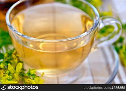 Herbal tea in a glass cup, fresh fresh flowers tutsan on the linen tablecloth background