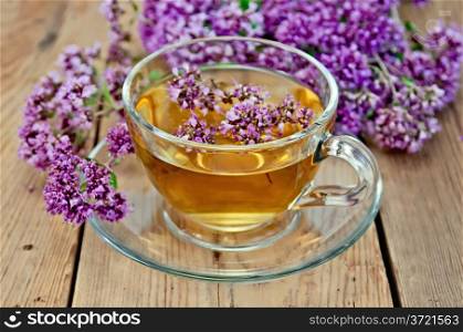 Herbal tea in a glass cup, fresh oregano flowers on a background of wooden boards
