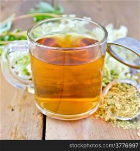 Herbal tea in a glass mug, metal sieve with dried flowers of meadowsweet, fresh flowers of meadowsweet on a wooden boards background