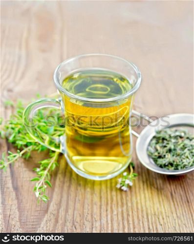 Herbal tea in a glass mug of thyme, metal strainer with dry leaves, fresh leaf on a wooden board background