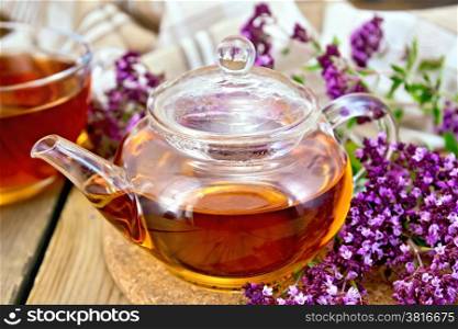 Herbal tea in a glass teapot and cup, fresh flowers oregano, napkin on wooden board