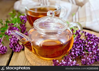 Herbal tea in a glass teapot and cup, fresh flowers oregano, napkin on wooden table