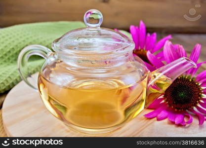 Herbal tea in a glass teapot, fresh flowers echinacea, napkin on a wooden boards background