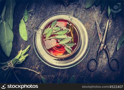Herbal tea , old scissors and sage leaves on dark rustic wooden background, top view. Retro toned