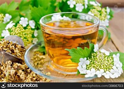 Herbal tea viburnum flowers in a glass cup, a metal strainer with dried flowers of Viburnum, Viburnum and fresh flowers on the background of wooden boards