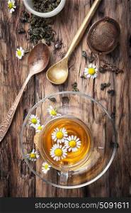 Herbal tea with chamomile. Glass cup with chamomile tea, tea strainer, chamomile flowers on rustic wooden background