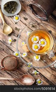 Herbal tea with chamomile. Glass cup with chamomile tea, tea strainer, chamomile flowers on a wooden background