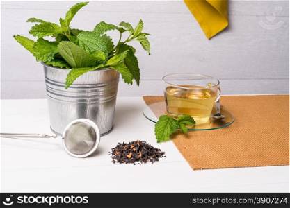 Herbal tea with melissa in a glass cup a green napkin on a light green wooden table top.