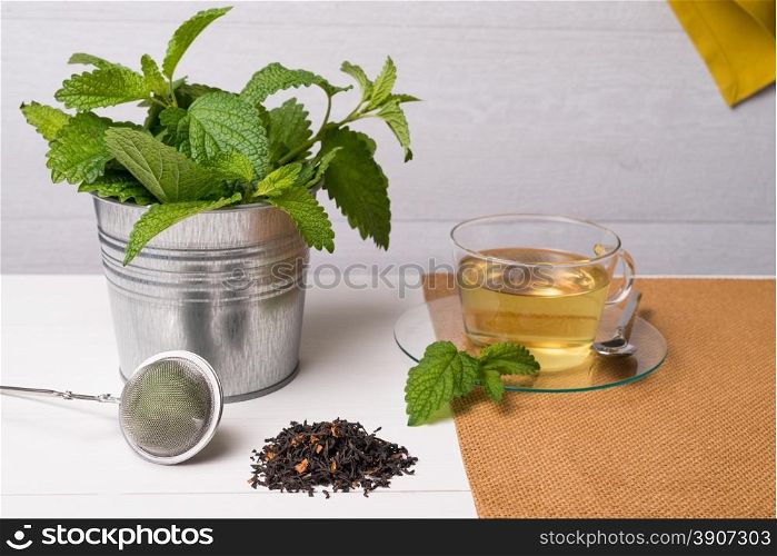 Herbal tea with melissa in a glass cup a green napkin on a white wooden table top.