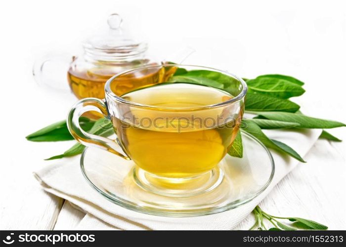 Herbal tea with sage in a glass cup on a towel on wooden board background