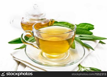 Herbal tea with sage in a glass cup on a towel on wooden board background