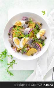 Herring and boiled potato salad with egg, capers and red onion. Top view