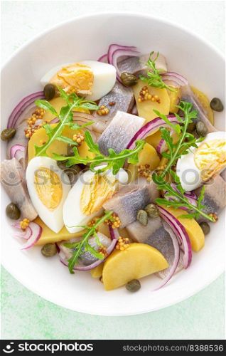 Herring and boiled potato salad with egg, capers and red onion. Top view