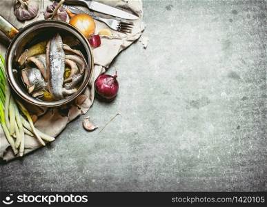 Herring fillets in a saucepan with spices. On a stone background.. Herring fillets in a saucepan with spices