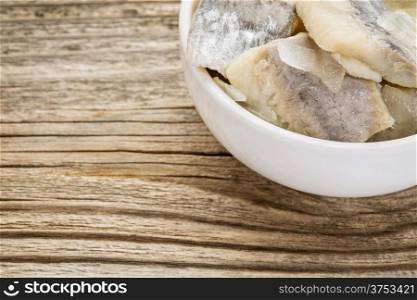 herring in wine sauce with onion and spices - white sauce dish on grained wood