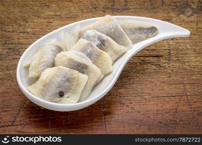 herring in wine sauce with onion and spices - white teardrop shaped bowl against rustic wood wood