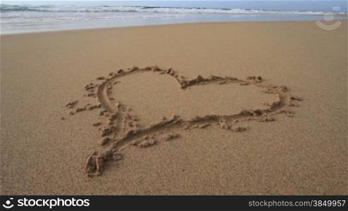 Herz am Sandstrand, das Wasser kommt sehr nahe ans Herz heran.