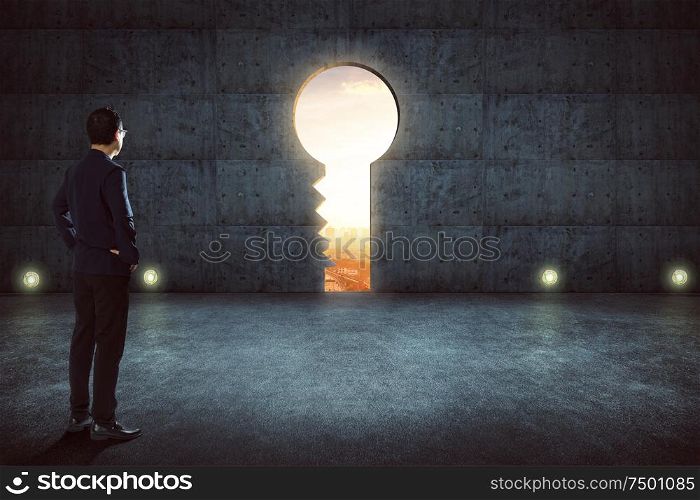 Hesitant businessman looking outside against concrete wall with key hole door ,sunrise scene city skyline outdoor view .