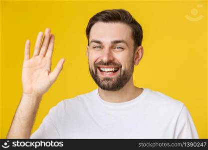 Hi, Hello. Portrait of happy friendly brown-haired man with small beard in white shirt waving hand to camera, welcoming with toothy smile. Hi, Hello. Portrait of happy friendly brown-haired man with small beard in white shirt waving hand to camera, welcoming with toothy smile.