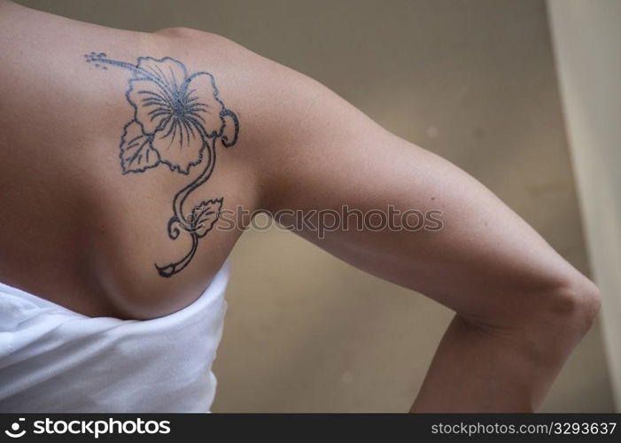 hibiscus flower tattoo on the shoulder of a young woman in a white undershirt