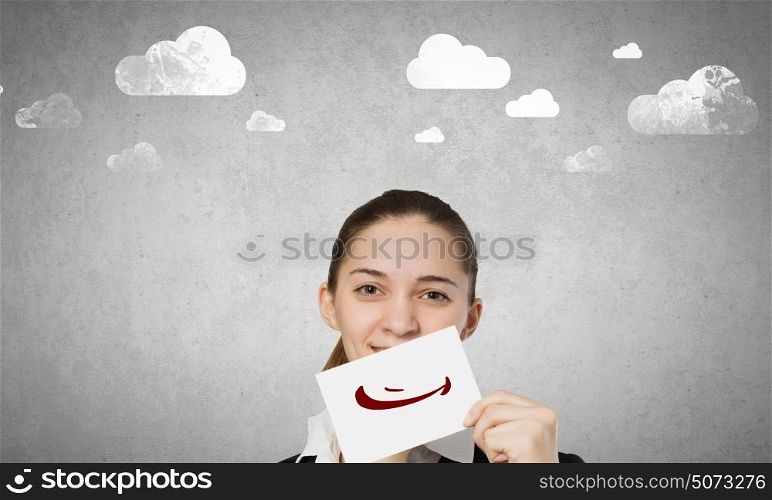 Hiding emotions. Young businesswoman holding paper with unhappy sad smiley