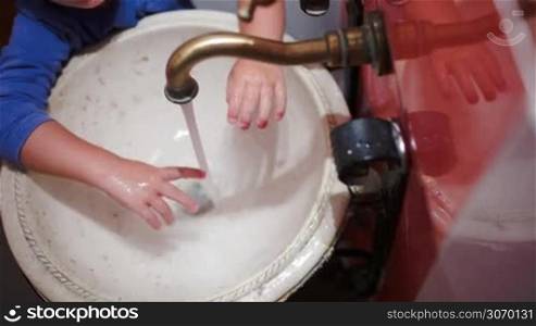 High angle and close-up shot of a little child washing hands in vintage sink and turning off the tap