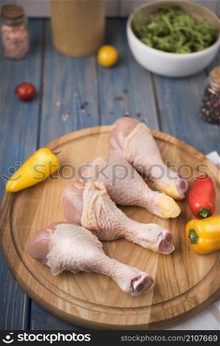 high angle chicken drumsticks wooden board with peppers tomatoes