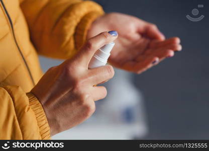 High angle close up unknown female person caucasian woman girl in jacket applying spray disinfection alcohol product hand disinfecting hands against virus bacteria health prevention spraying outdoor