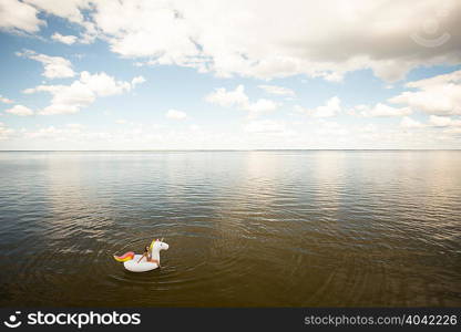 High angle distant view of young woman sitting on inflatable unicorn in sea, Santa Rosa Beach, Florida, USA