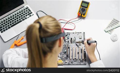 high angle female technician with soldering iron electronics motherboard