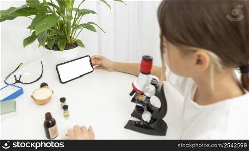 high angle girl looking into microscope holding smartphone