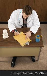 High angle of mid-adult Caucasian male doctor at desk writing.