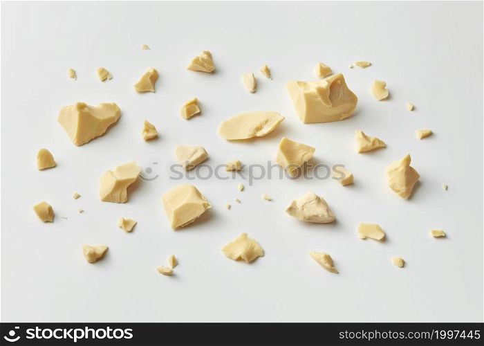 High angle of organic pure cocoa butter in chunks and crumbs placed on white background. Scattered pieces of solid Theobroma oil