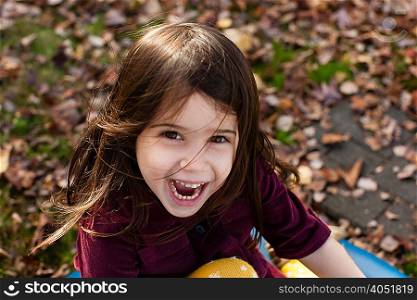 High angle portrait of young girl among autumn leaves looking at camera open mouthed smiling