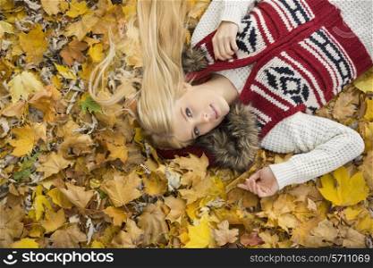 High angle portrait of young woman lying on autumn leaves in park